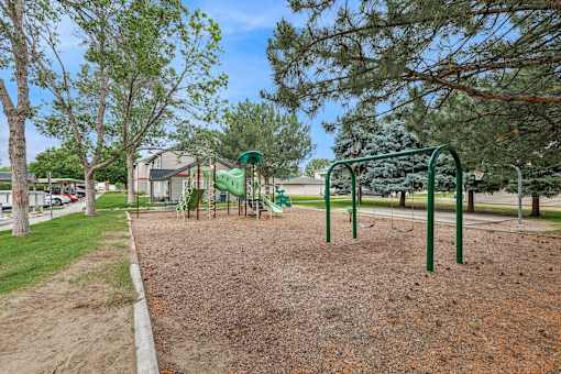 A playground with a green swing set and a red dirt ground.