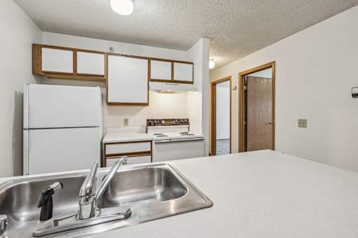 A kitchen with a white fridge, sink, and countertops.