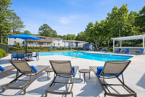 A pool surrounded by chairs and trees.
