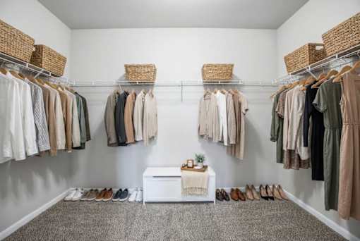 A white bench with a plant on it sits in the middle of a room with clothes hanging on racks on both sides.