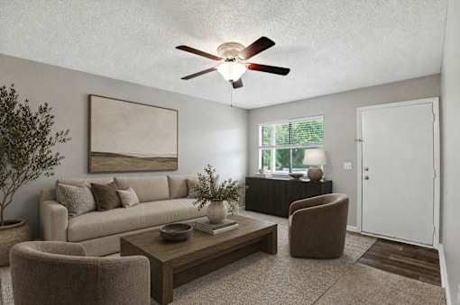 A living room with a beige couch, a brown armchair, a coffee table, and a ceiling fan.