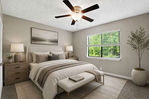 A bedroom with a large bed, a ceiling fan, and a window showing greenery outside.