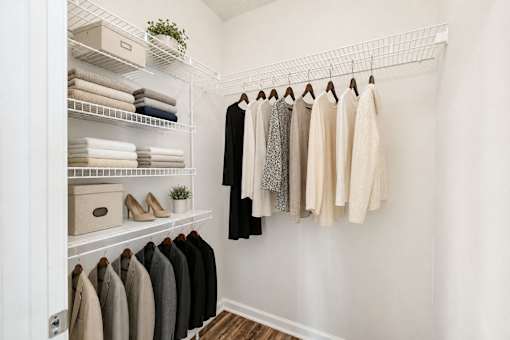 A white closet with clothes hanging and towels folded on shelves.