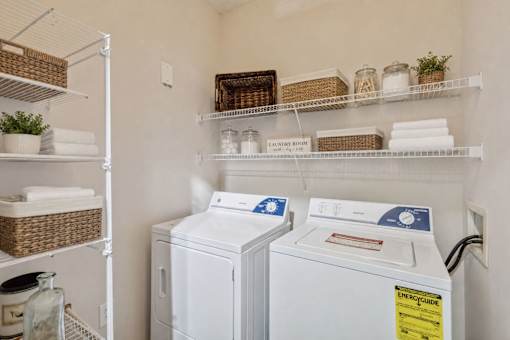 A laundry room with two washing machines and shelves with baskets and plants.