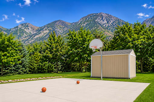 A basketball court with a basketball hoop and two balls on the ground at Slate Canyon Apartments, Provo