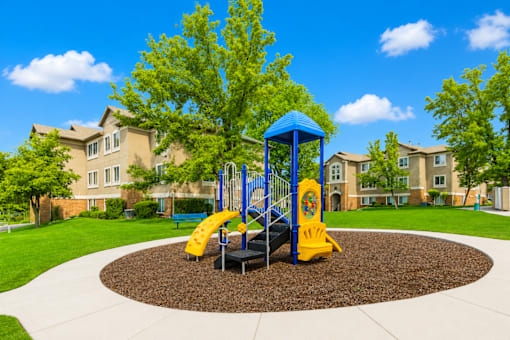 A playground with a blue and yellow slide in the middle of a circular play area at Slate Canyon Apartments, Utah, 84606