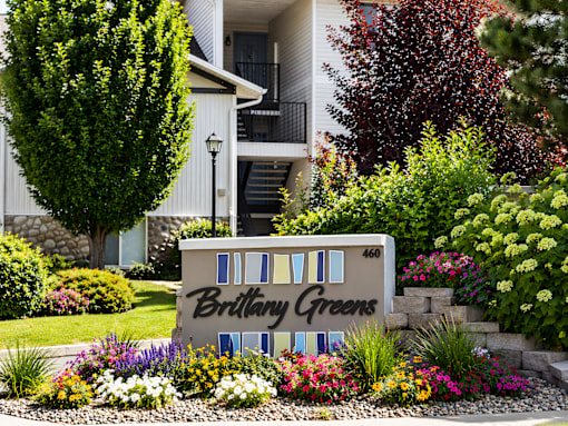 A sign for Brillay Greens is surrounded by flowers and plants.