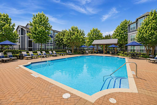A large outdoor swimming pool surrounded by trees and lounge chairs.