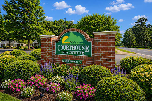 A sign for Courthouse Senior Apartments is surrounded by flowers and greenery.