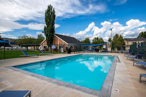 A large outdoor swimming pool surrounded by a fence and lounge chairs.