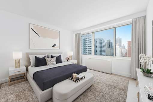 A bedroom with a large bed and a city view through the window.