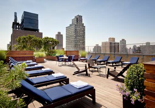 A rooftop patio with blue lounge chairs and wooden flooring.