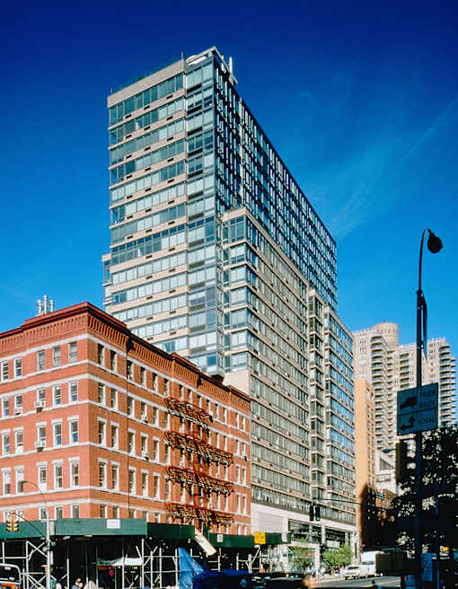 A tall glass building stands next to a shorter brick building with a green awning in front of it.