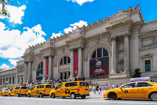 A row of yellow taxis are parked in front of a large building.