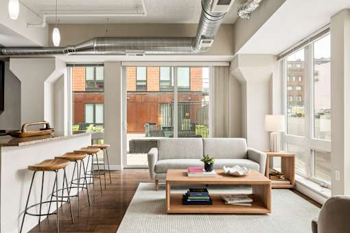 A modern living room with a grey couch, a wooden coffee table, and a bar area with stools.