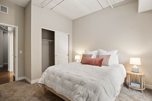 A bedroom with a large bed and a small table with a lamp.