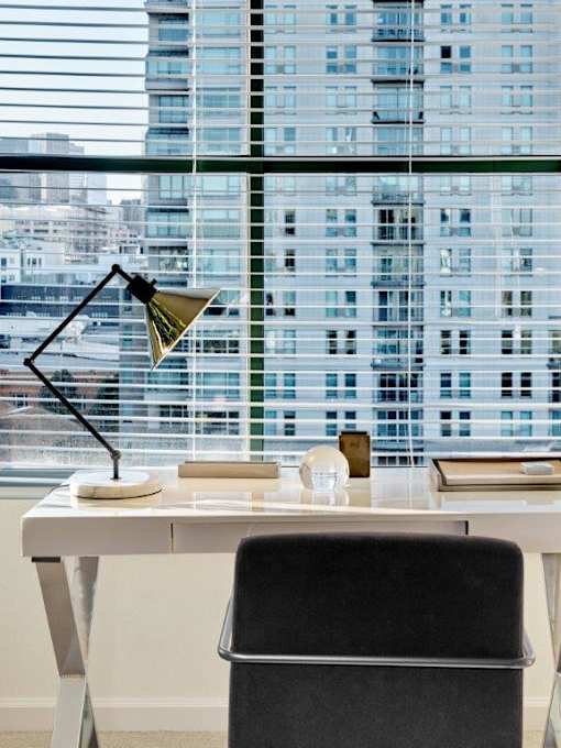 A black chair sits in front of a desk with a lamp on it.
