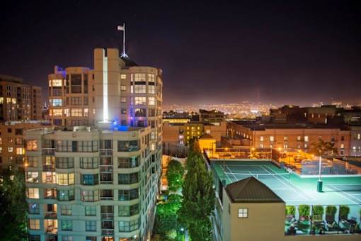 A tall building with a flag on top is lit up at night.