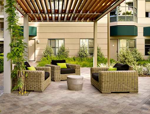 A patio with a wooden roof and wicker furniture.