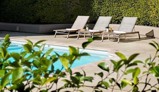 A pool surrounded by chairs and greenery.
