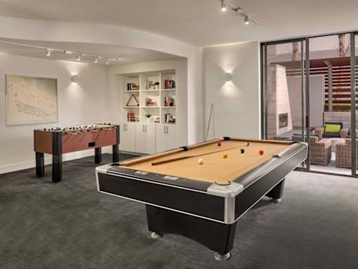 A pool table is in the middle of a room with a bookshelf and a painting on the wall.