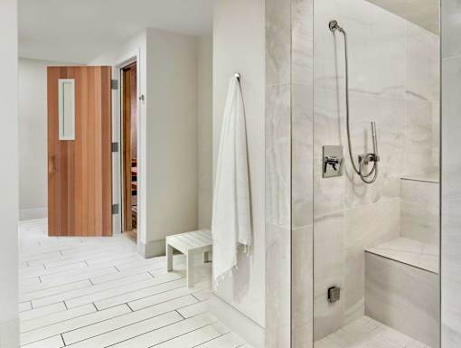 A white tiled bathroom with a wooden door and a white bench.