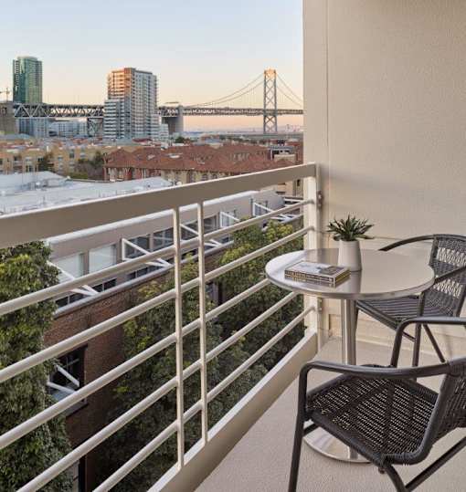 A balcony with a table and chairs overlooking a cityscape.
