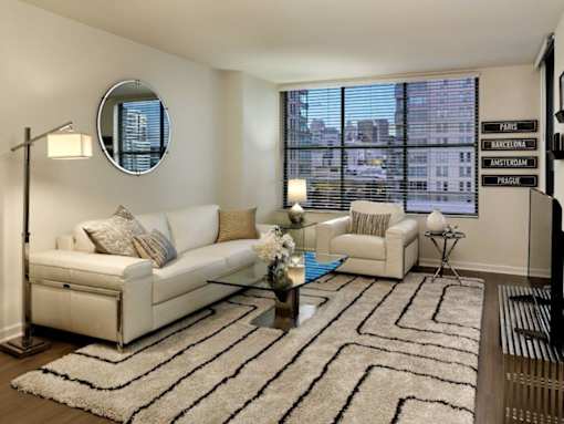 A living room with a white couch, a round mirror, and a rug with a black and white pattern.
