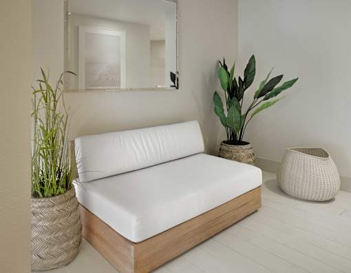 A white sofa with wooden frame and a potted plant beside it.
