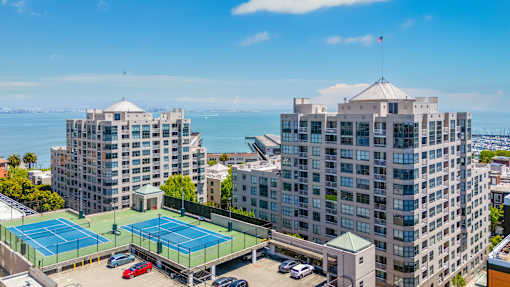 A tennis court is located between two buildings.