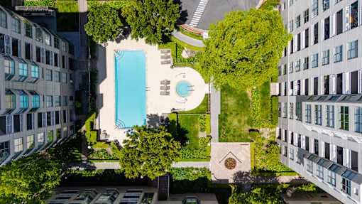 A swimming pool is surrounded by trees and grass in a courtyard.
