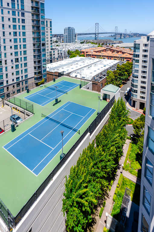 Two tennis courts on a rooftop with trees and buildings around.