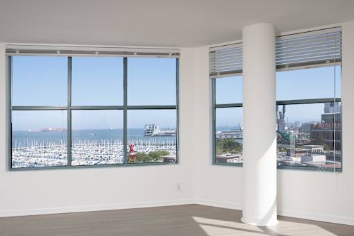 A white column stands in a room with two windows overlooking a marina.