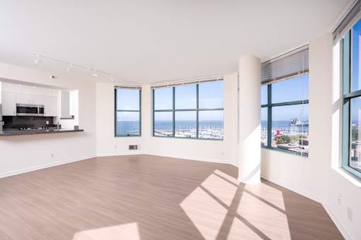 A spacious room with wooden floors and large windows overlooking a cityscape.