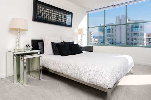 A bedroom with a large bed, a table with a lamp, and a framed picture on the wall.