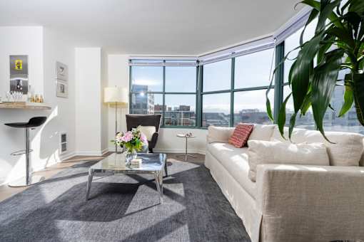 A living room with a white couch, a glass coffee table, and a large window.