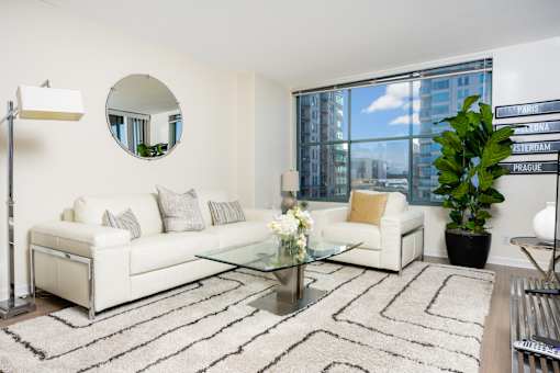 A living room with a white couch, a glass coffee table, and a mirror on the wall.