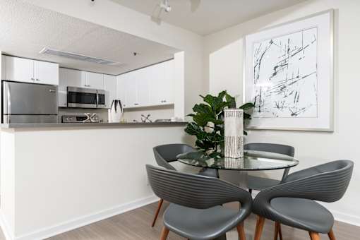 A modern kitchen with a glass dining table and grey chairs.