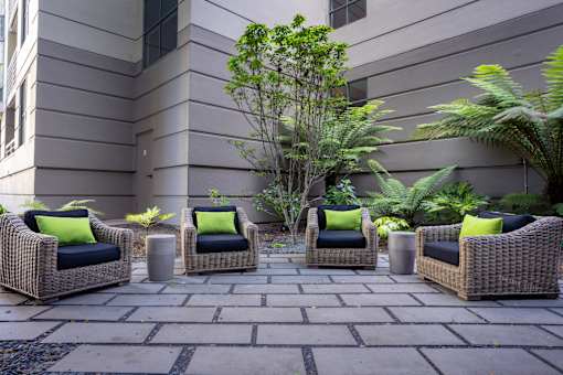 Four wicker chairs with green pillows are arranged on a patio.