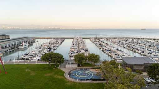A marina with boats docked in the water and a circular fountain in the foreground.
