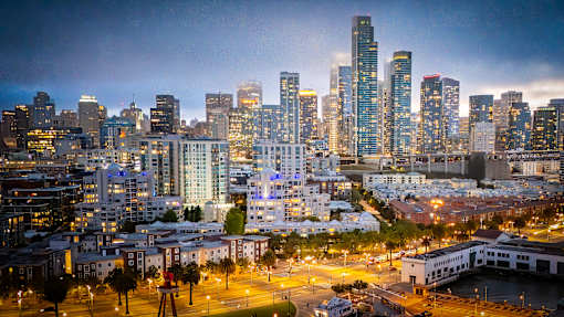A cityscape at dusk with buildings illuminated against a darkening sky.