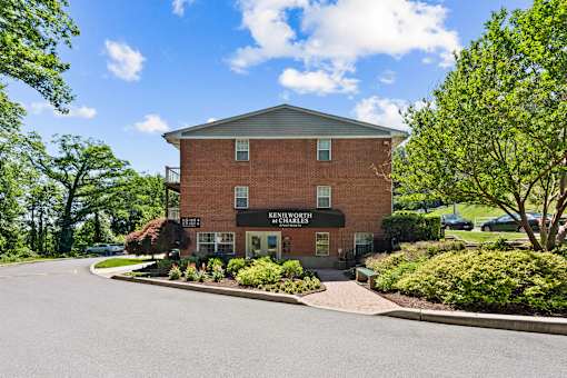 A building with a sign that reads "Kingdom Hall" sits in front of a tree and bushes.