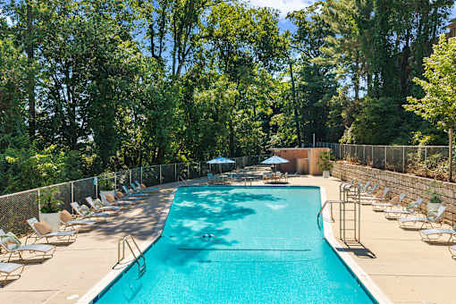 A large swimming pool surrounded by trees and chairs.