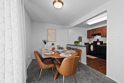 A dining room with a table set for two and a kitchen area in the background.