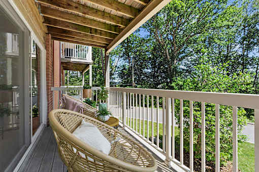 A wicker chair is on a porch with a view of trees.