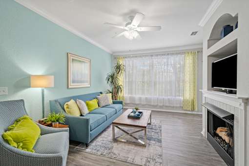 A living room with a grey couch, a green chair, a coffee table, a fireplace, and a ceiling fan at The Grand Reserve at Tampa Palms Apartments, Tampa, FL