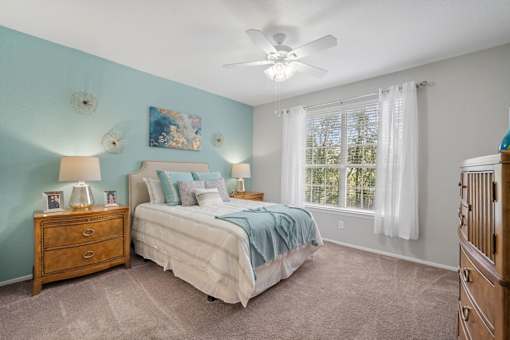 A bedroom with a bed, dresser, and ceiling fan at The Grand Reserve at Tampa Palms Apartments, Tampa, FL
