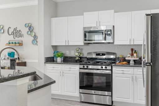 A kitchen with white cabinets and a black countertop at The Grand Reserve at Tampa Palms Apartments, Tampa