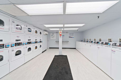 Community laundry center with white washers and dryers and a black rug on the floor at Mount Ridge Apartments, Baltimore, MD