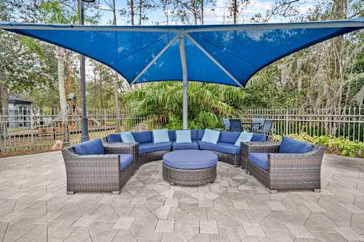 A patio with a blue canopy and grey wicker furniture at The Grand Reserve at Tampa Palms Apartments, Tampa, 33647